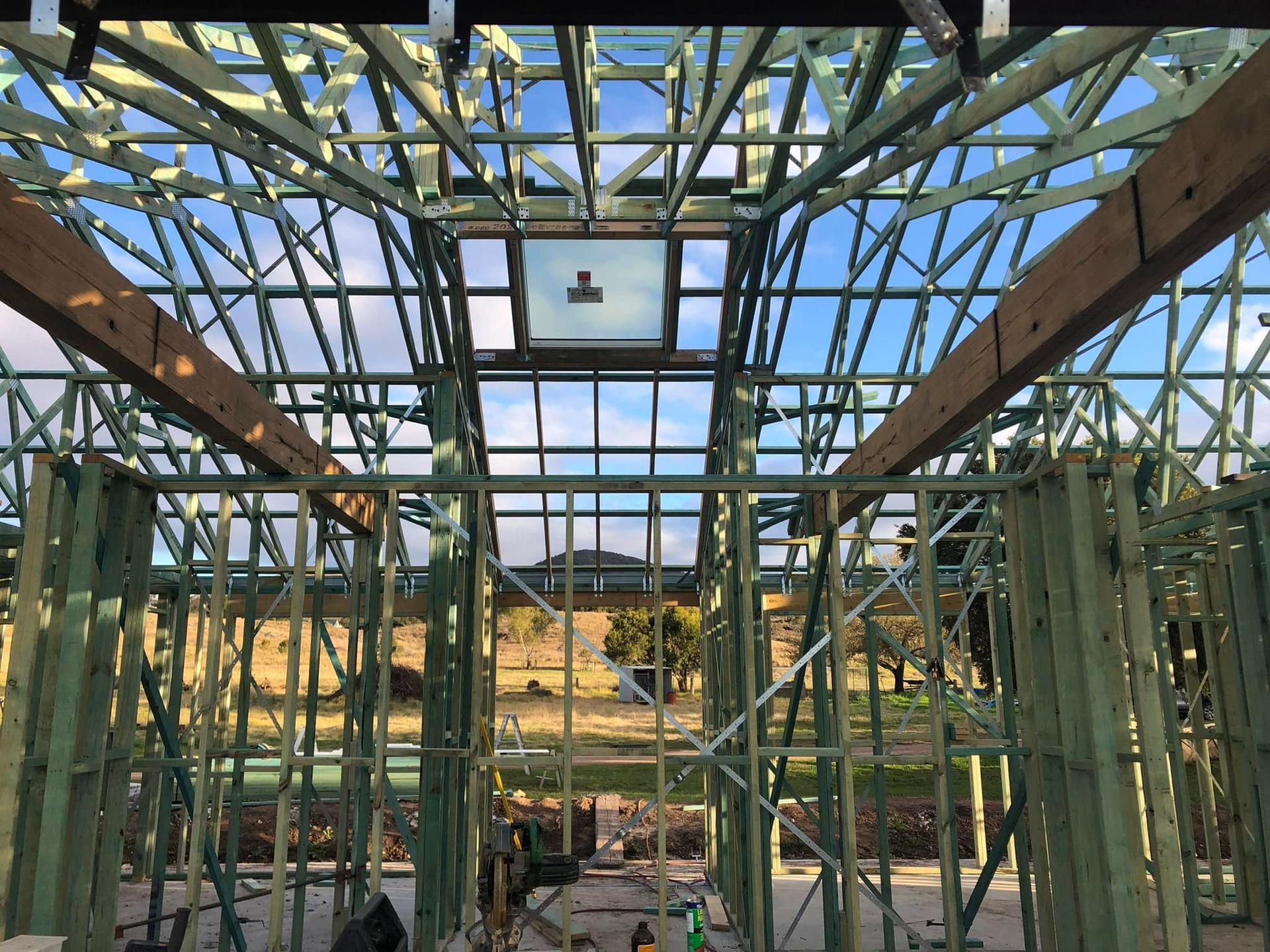 The sun is shining through the windows of a wooden house under construction — Trussted Frames & Trusses In Taminda, NSW