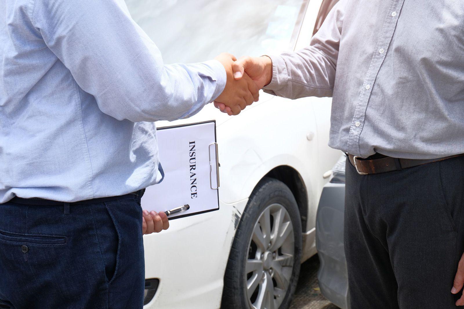 Two men shaking hands in front of a white car