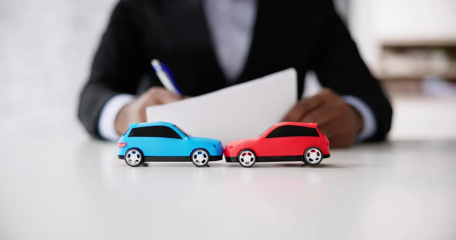 A man is signing a document next to two toy cars on a table.