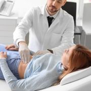 A doctor examines a woman 's stomach while she is laying on a bed