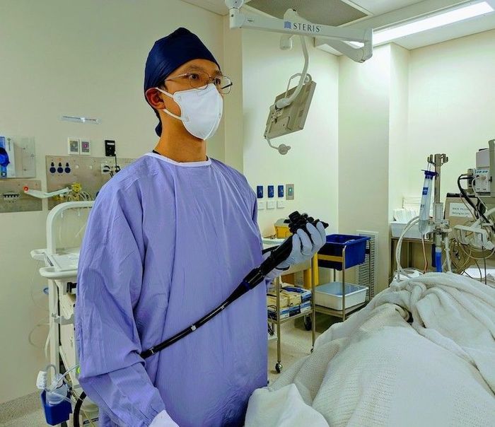 A surgeon wearing a mask and gown is holding an endoscope in an operating room