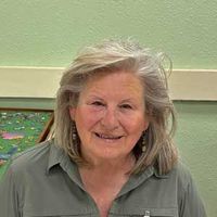 Smiling woman in a green shirt seated indoors against a light green wall