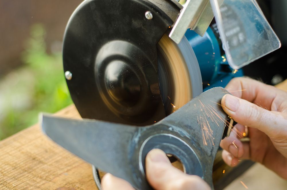 Hands Sharpening A Lawnmower Blade With A Bench Grinder — Jack Too You Mobile Servicing and Repairs In Sunshine Coast, QLD