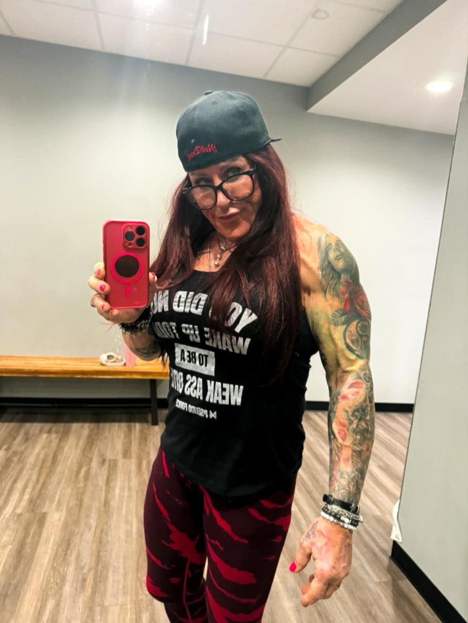 Woman in gym outfit holding a phone, flexing a muscular arm with tattoos.