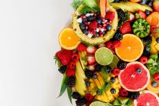 Assortment of colorful fruits, including strawberries, oranges, and a pineapple bowl, on a white surface.