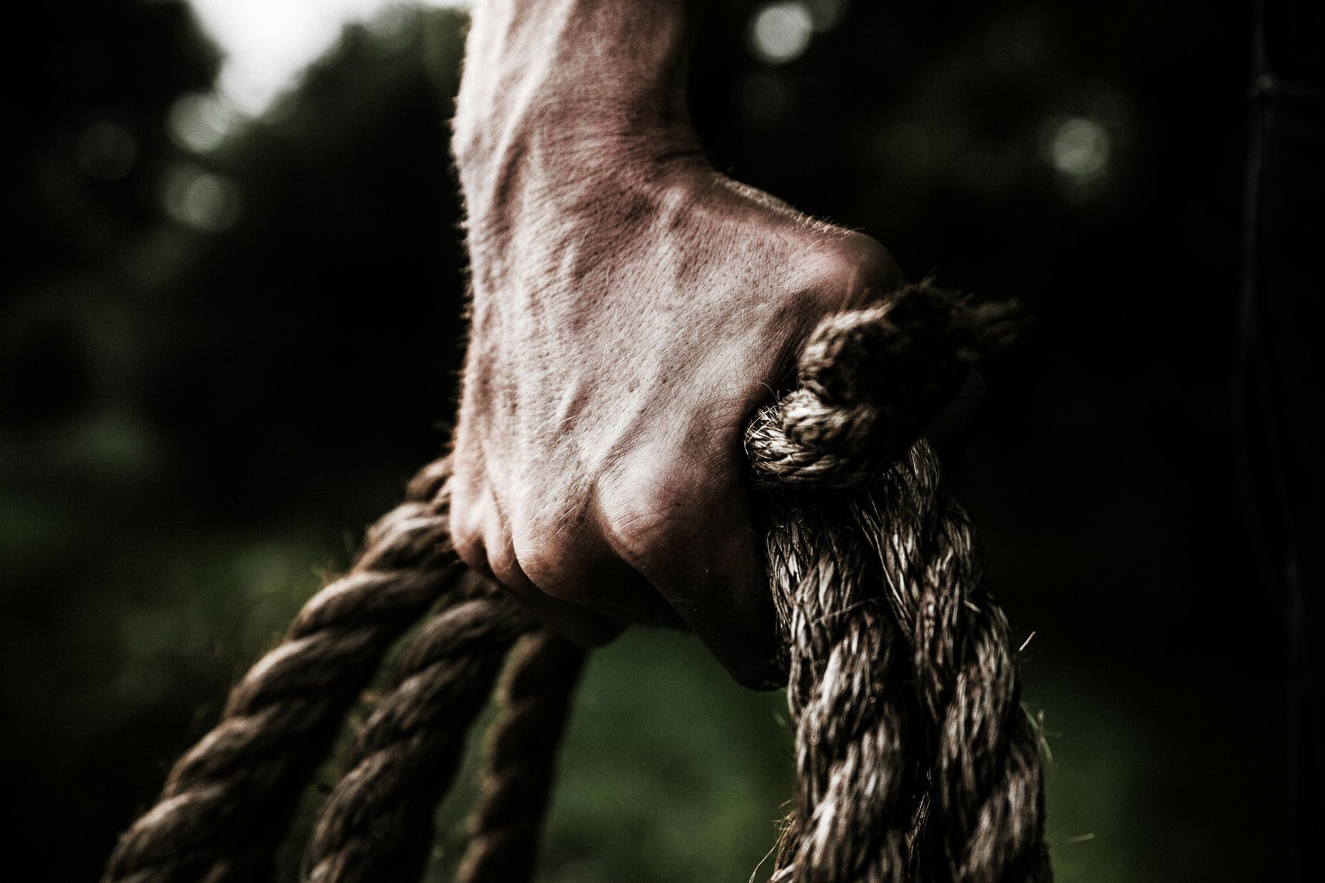 Hand gripping a thick, rough rope outdoors, dark background.