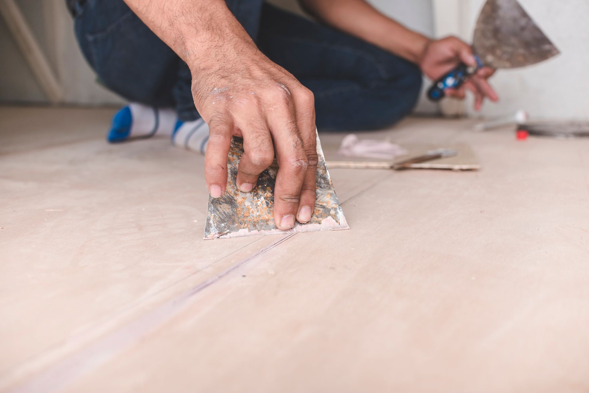 A man is kneeling on the floor using a spatula.