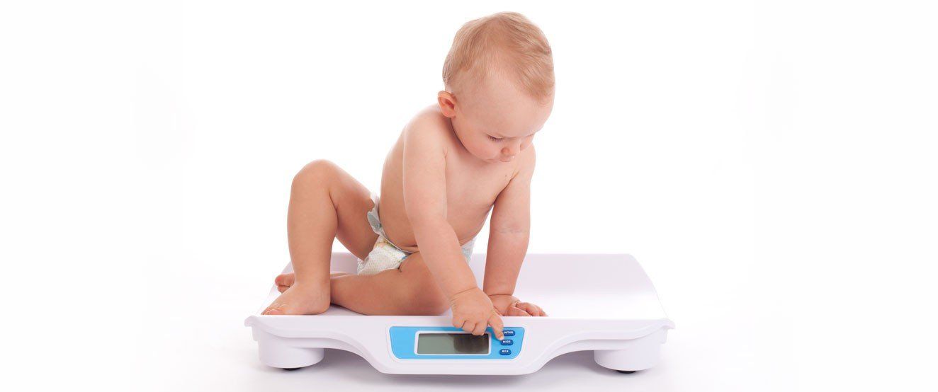 A baby in a diaper is sitting on a scale.