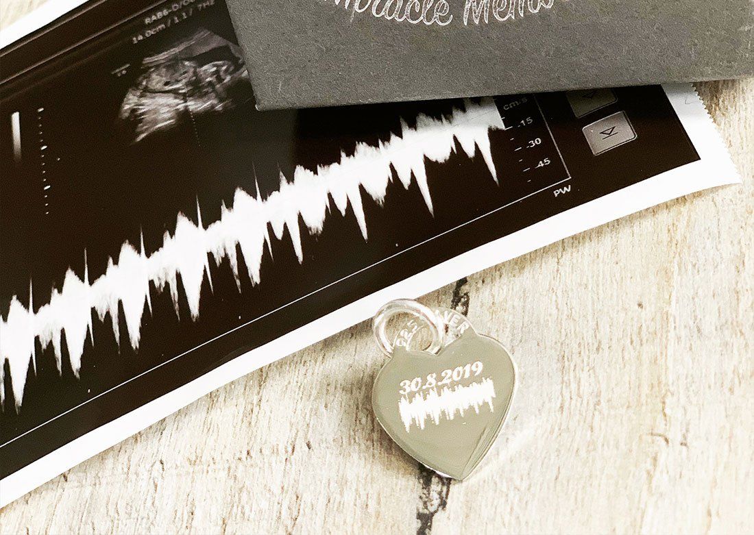 A heart shaped pendant is sitting next to an ultrasound of a baby