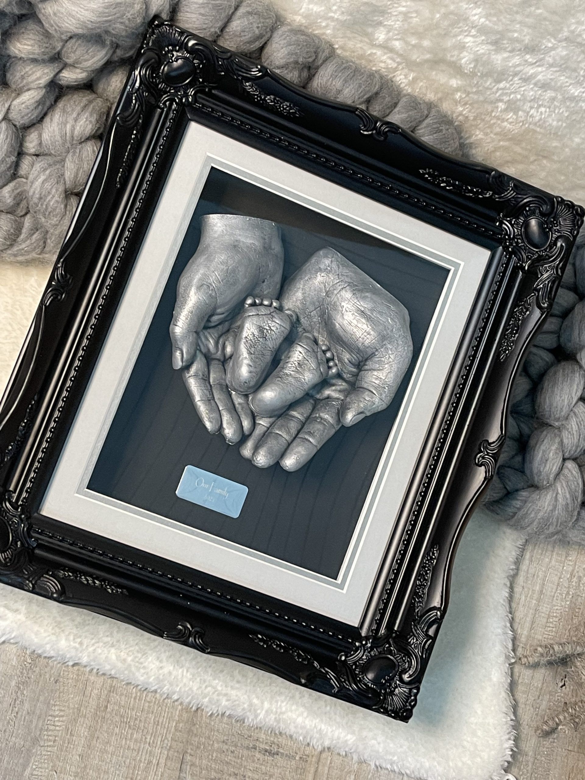 A picture of two hands holding a baby 's feet in a frame.