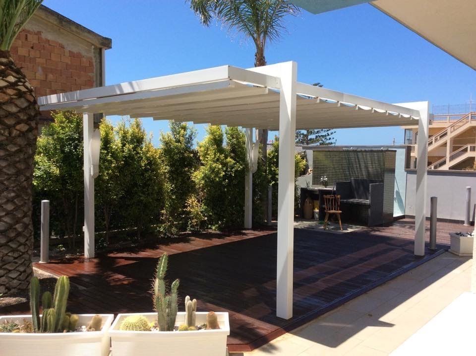 Un pergolato bianco è posto in cima a una terrazza di legno accanto a una palma.