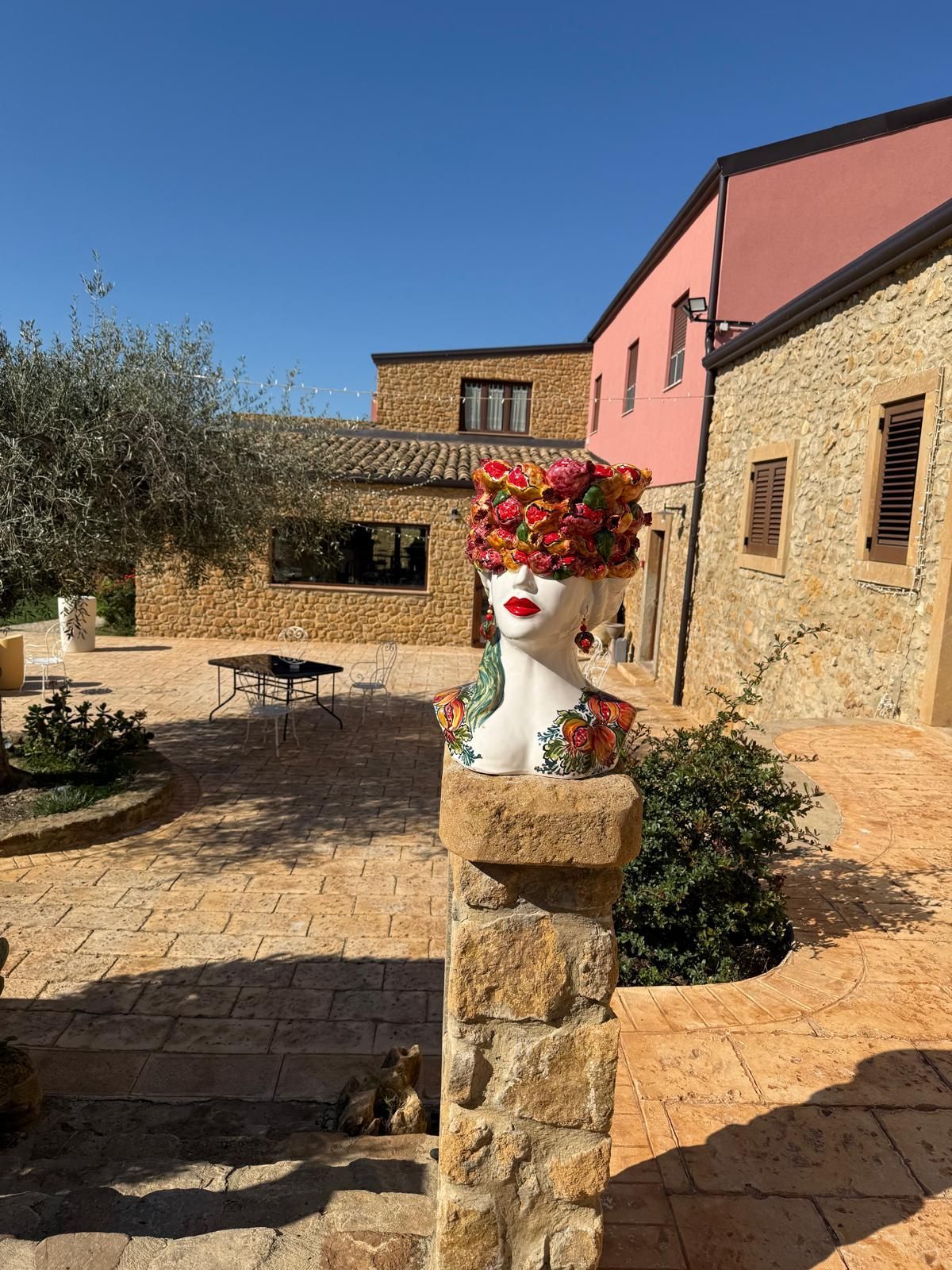 Una statua di una donna con dei fiori in testa è seduta su un pilastro di pietra di fronte a un edificio.