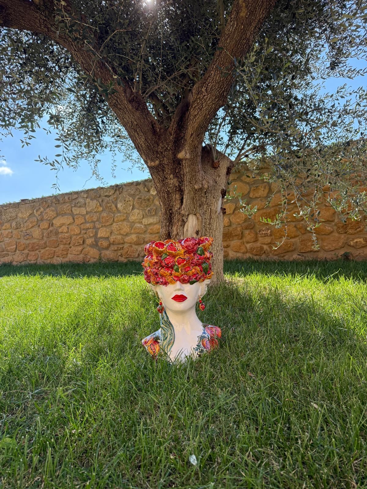 Una statua raffigurante una testa di donna è seduta sull'erba sotto un albero.