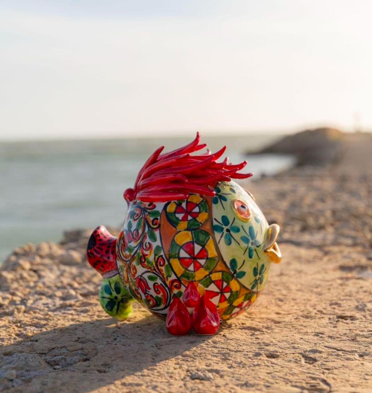 Un salvadanaio colorato con una criniera rossa si trova sulla spiaggia