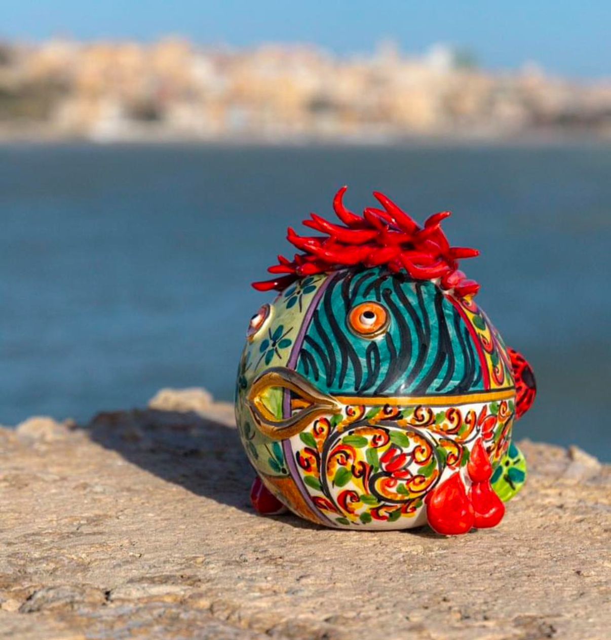 Un pesce di ceramica colorato con i capelli rossi è seduto su una roccia vicino all'acqua
