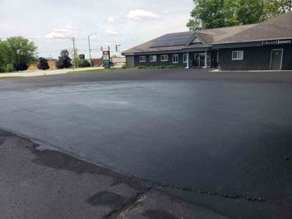 A black building with solar panels on the roof is sitting next to a large asphalt parking lot.