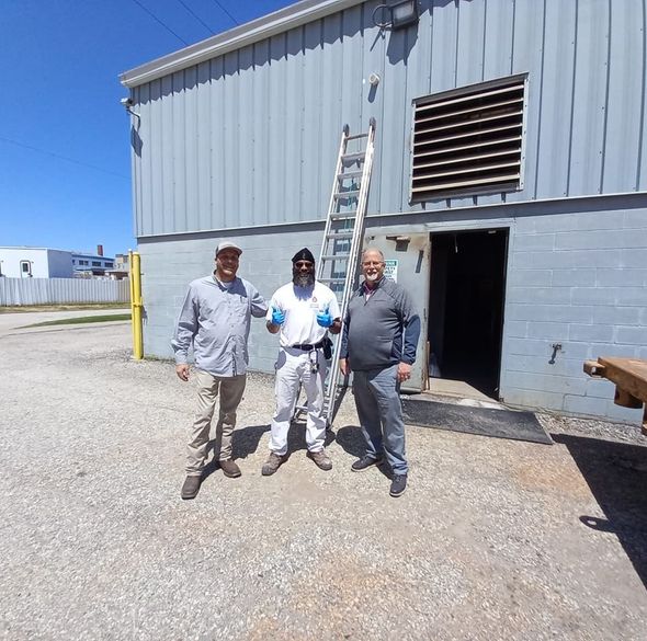 Three men standing outside a blue building. One in white paint suit gives a thumbs up. Ladder leans against the building.