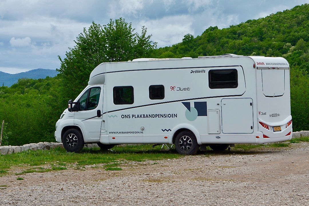 Op een betaalde vrije plek Een witte camper staat geparkeerd op een grindterrein voor een berg.