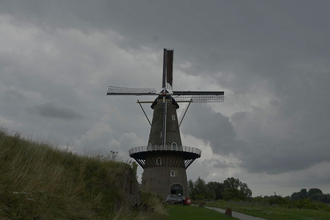 Een grote windmolen staat op de top van een met gras begroeide heuvel.