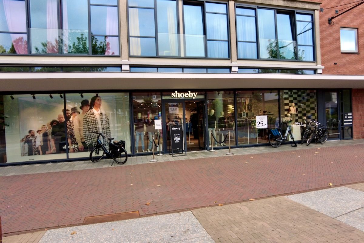 Speciaal voor Petra Voorgevel van een schoenenwinkel met glazen ramen, fietsen en een stenen pad.