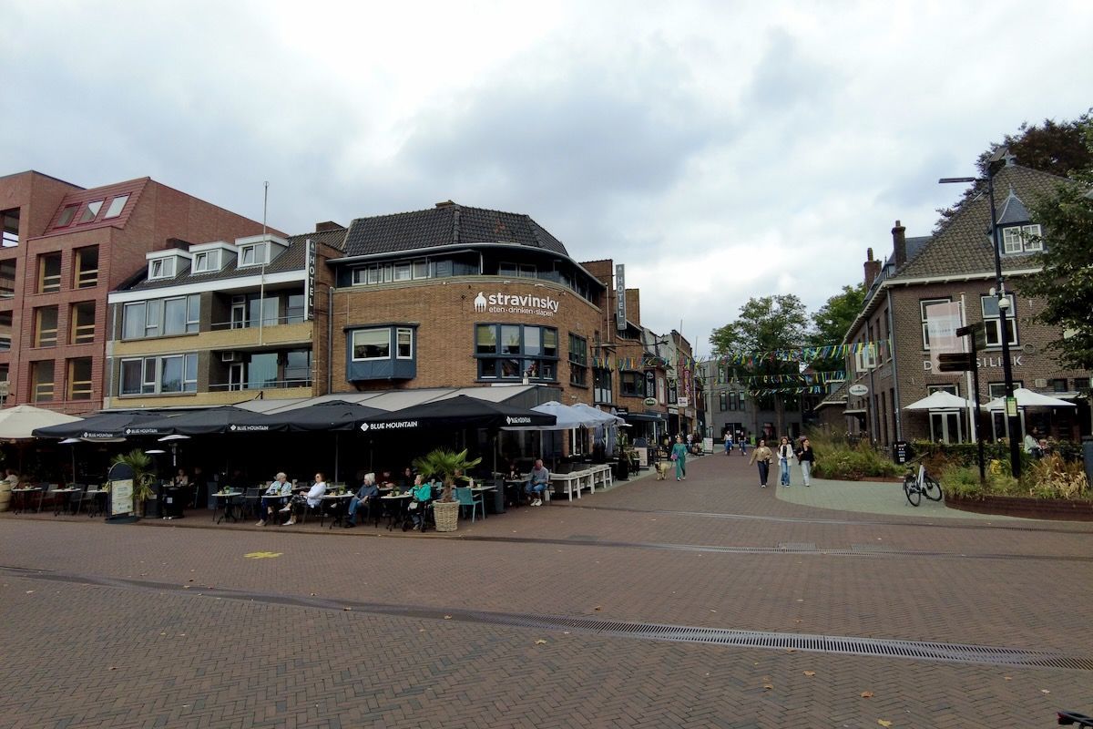 Organisator buiten lunch Straatbeeld met bakstenen gebouwen, een terras bij een restaurant en voetgangers op een bewolkte dag.