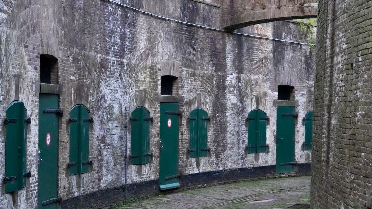 Een rij groene deuren in een bakstenen muur.