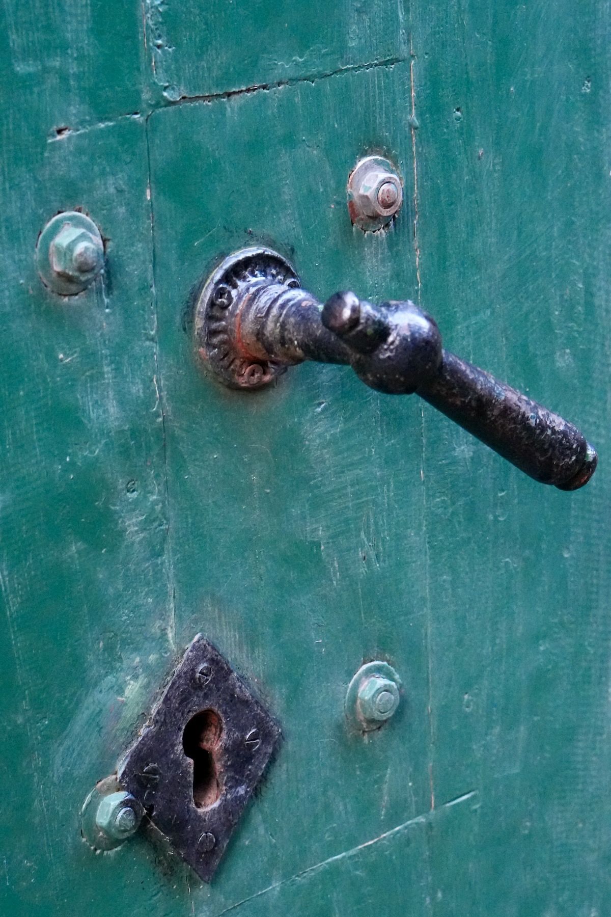 Een close-up van een deurklink en sleutelgat op een groene deur.