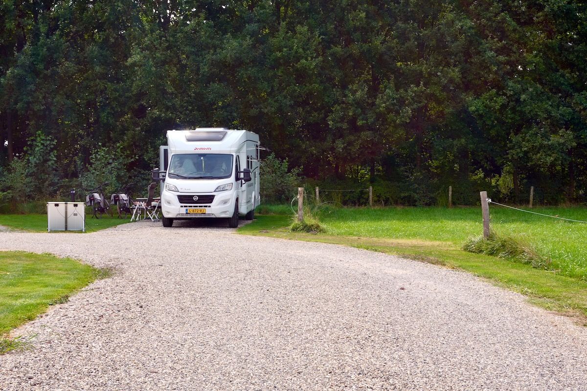 Op de kop Een witte camper geparkeerd op een grindpad bij een camping. Bomen op de achtergrond.