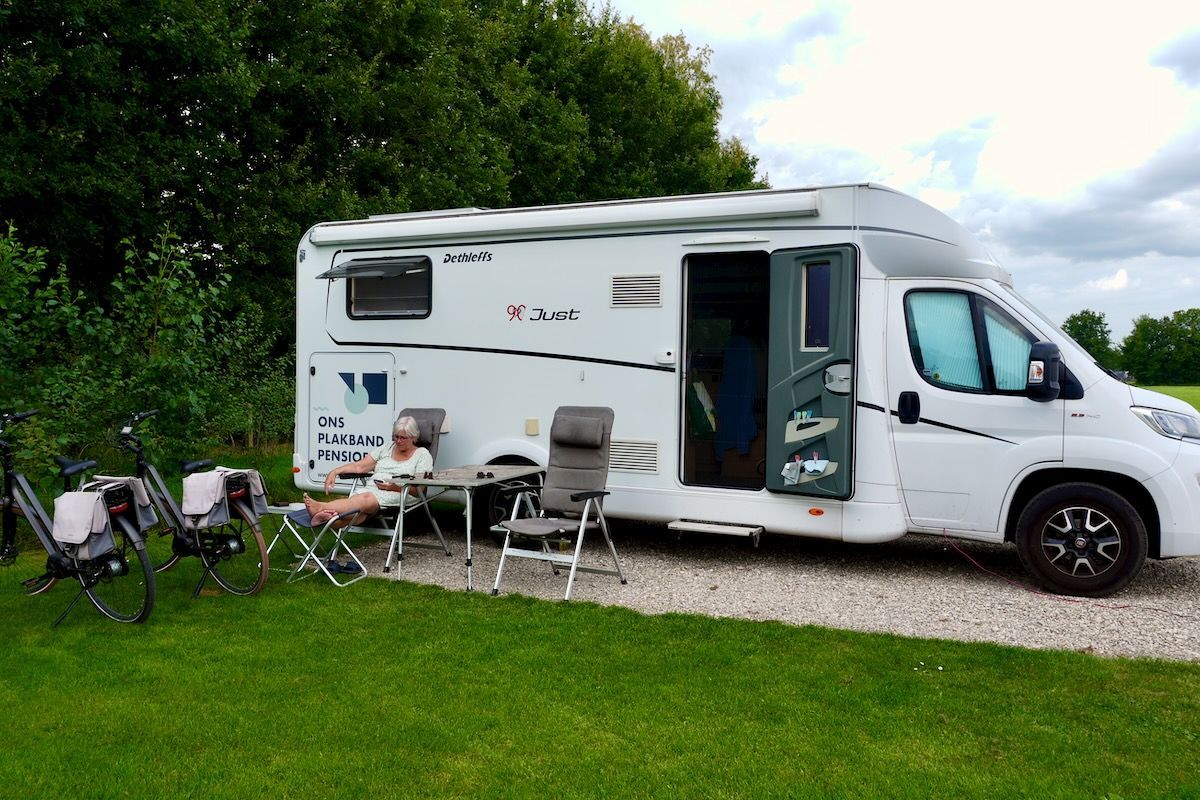 Mooi plekje Een persoon zit buiten voor een witte camper op een grasveld met fietsen.