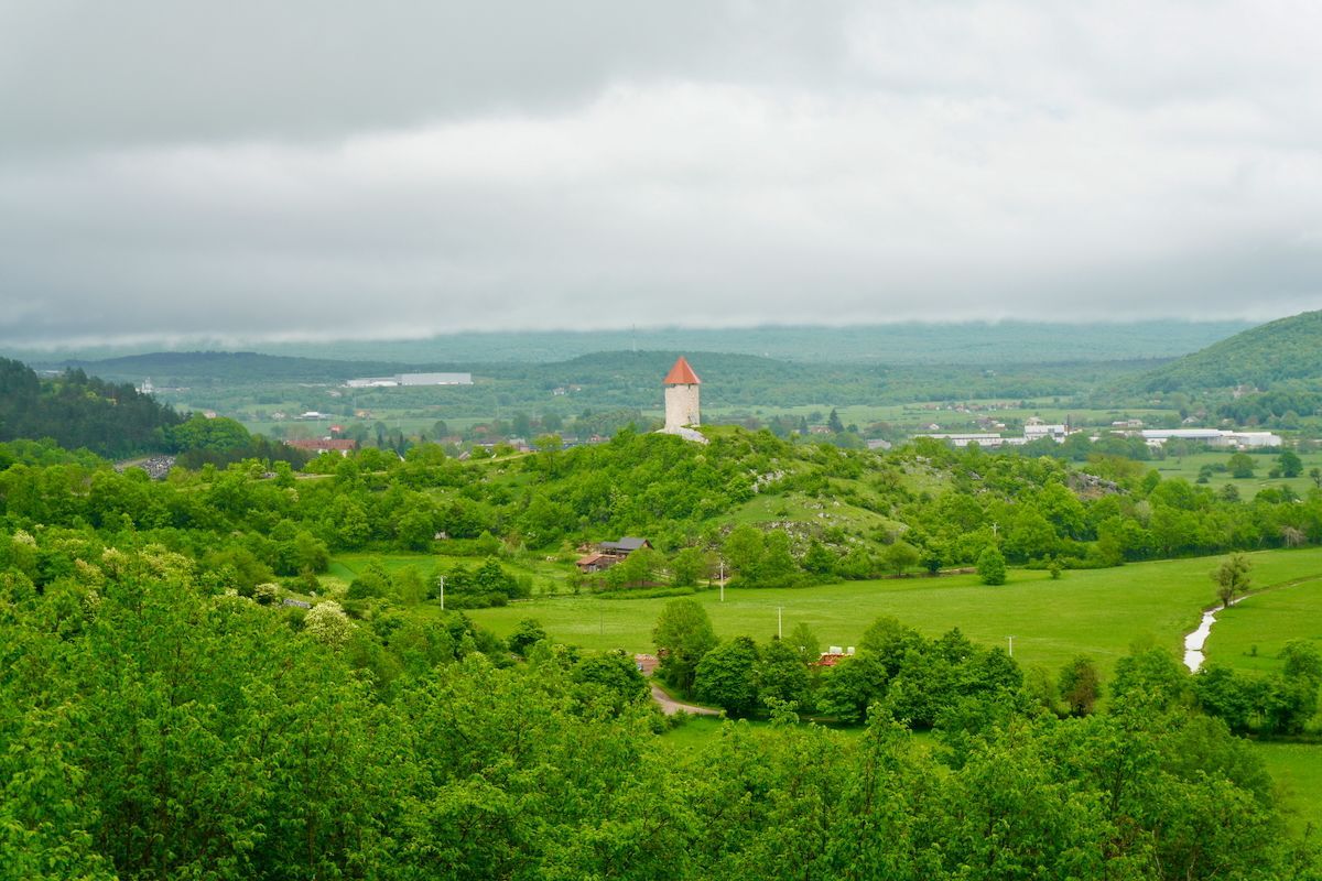 Stari grad Perušić Een kasteel op de top van een heuvel, midden in een weelderige groene vallei, omgeven door bomen.