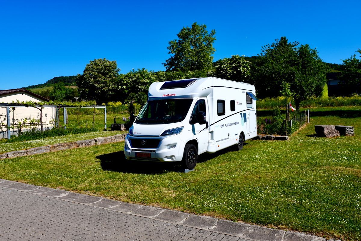 Plek op het gazon Een witte camper staat geparkeerd in een grasveld.