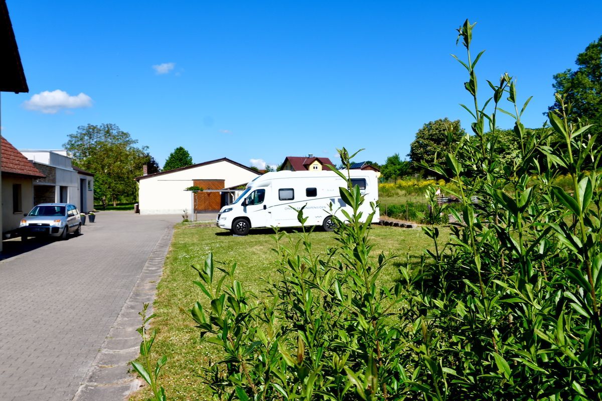 Bijna geen wolkje aan de lucht Een camper staat geparkeerd op een grasveld voor een gebouw
