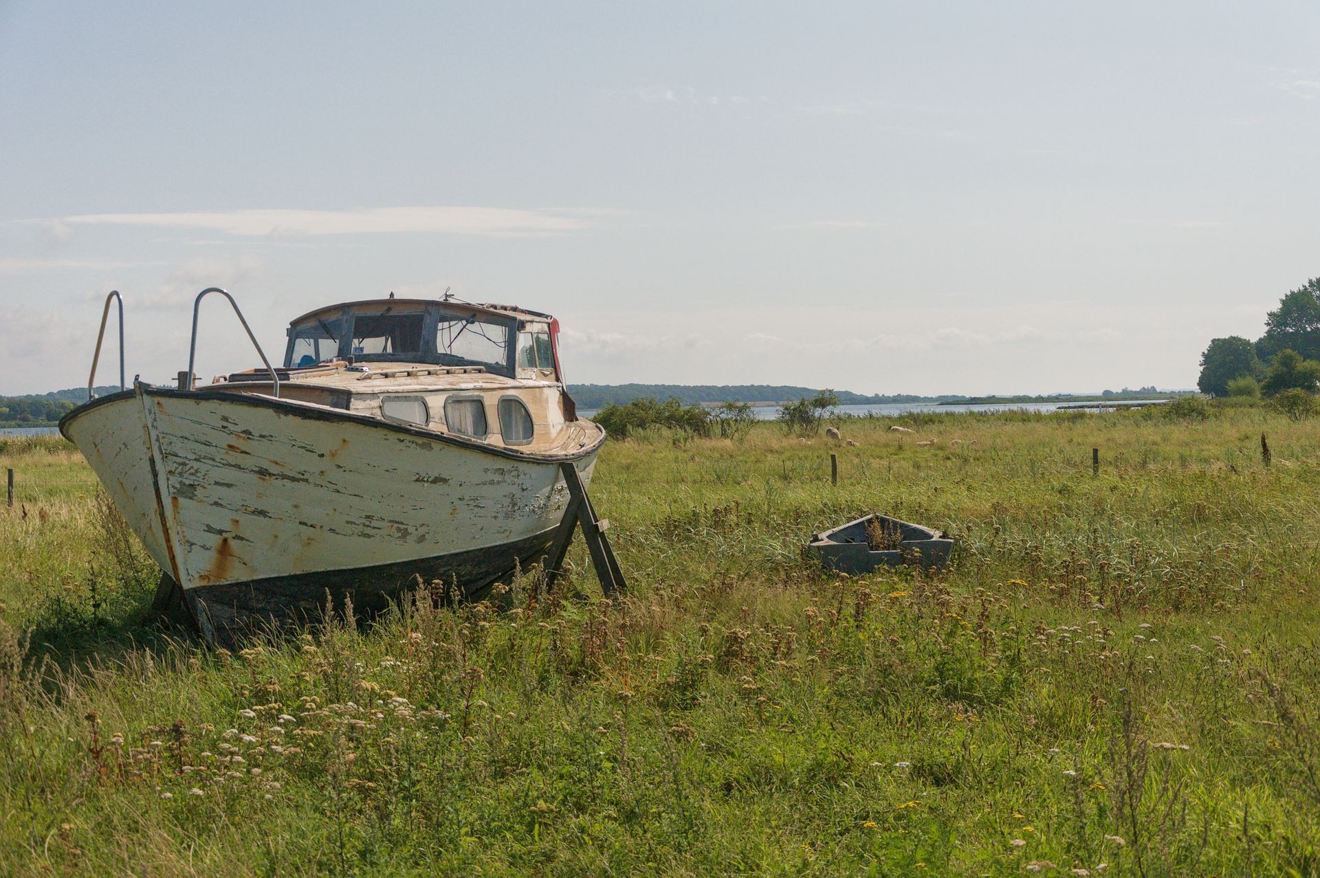 An old boat sits in a grassy field under a clear sky.