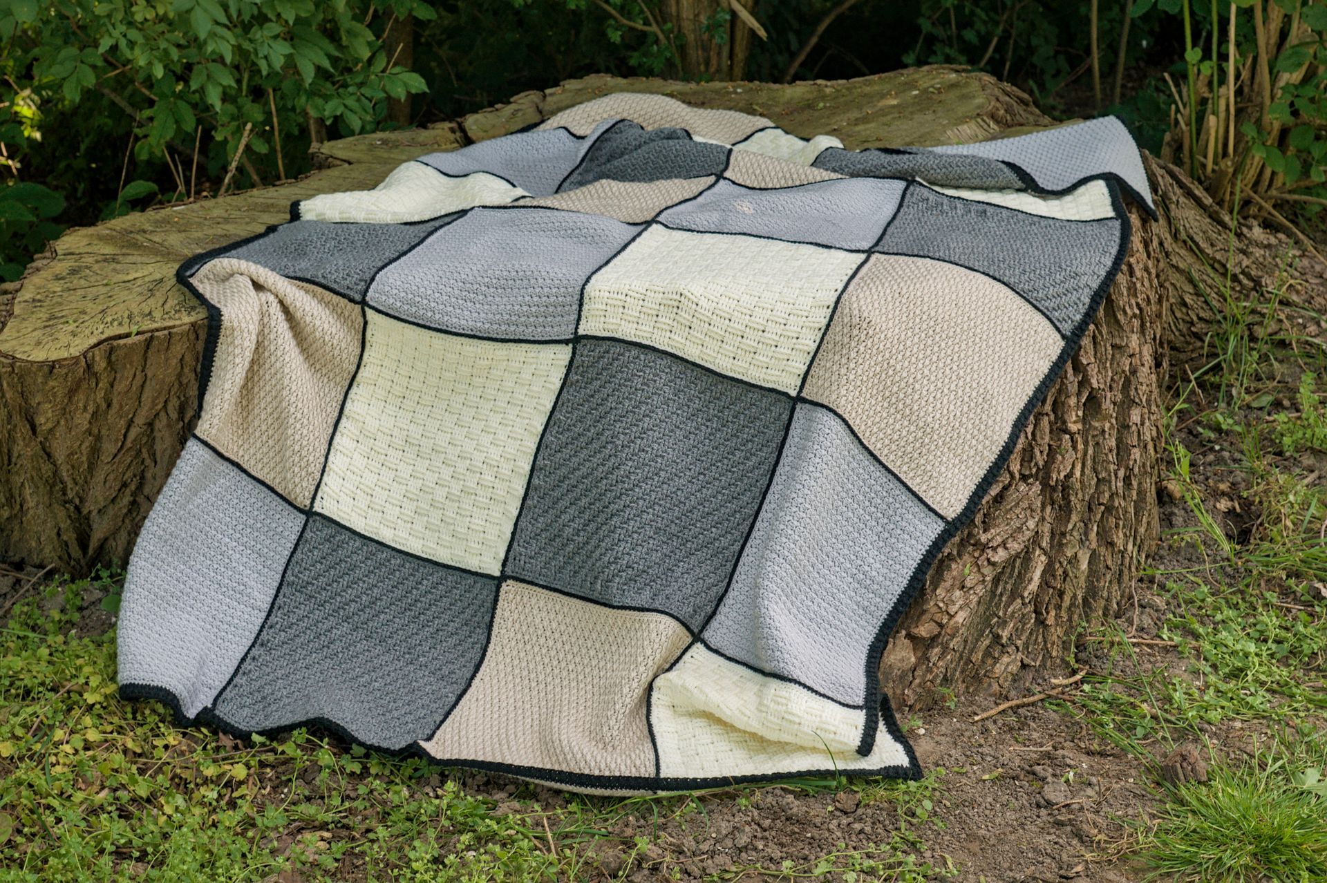 Een patchworkdeken gedrapeerd over een hooibaal in een grasrijke buitenomgeving.