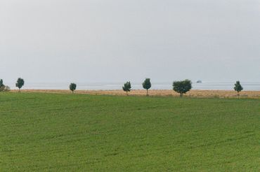 Witte camper geparkeerd op een rotsachtige, onverharde plek naast groene heuvels onder een blauwe hemel.