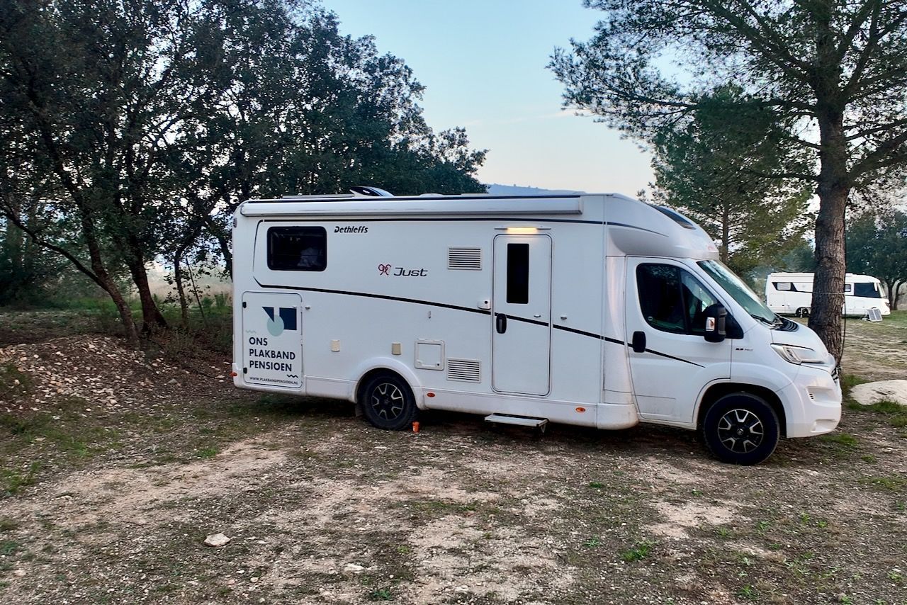 Witte camper geparkeerd op een onverharde weg vlakbij bomen.