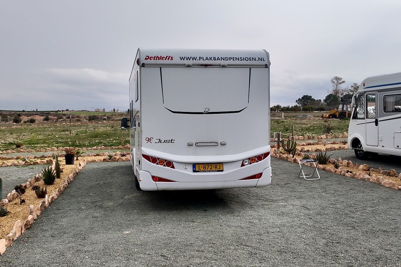 Witte camper geparkeerd op grind, met op de achtergrond een veld en een bewolkte hemel.