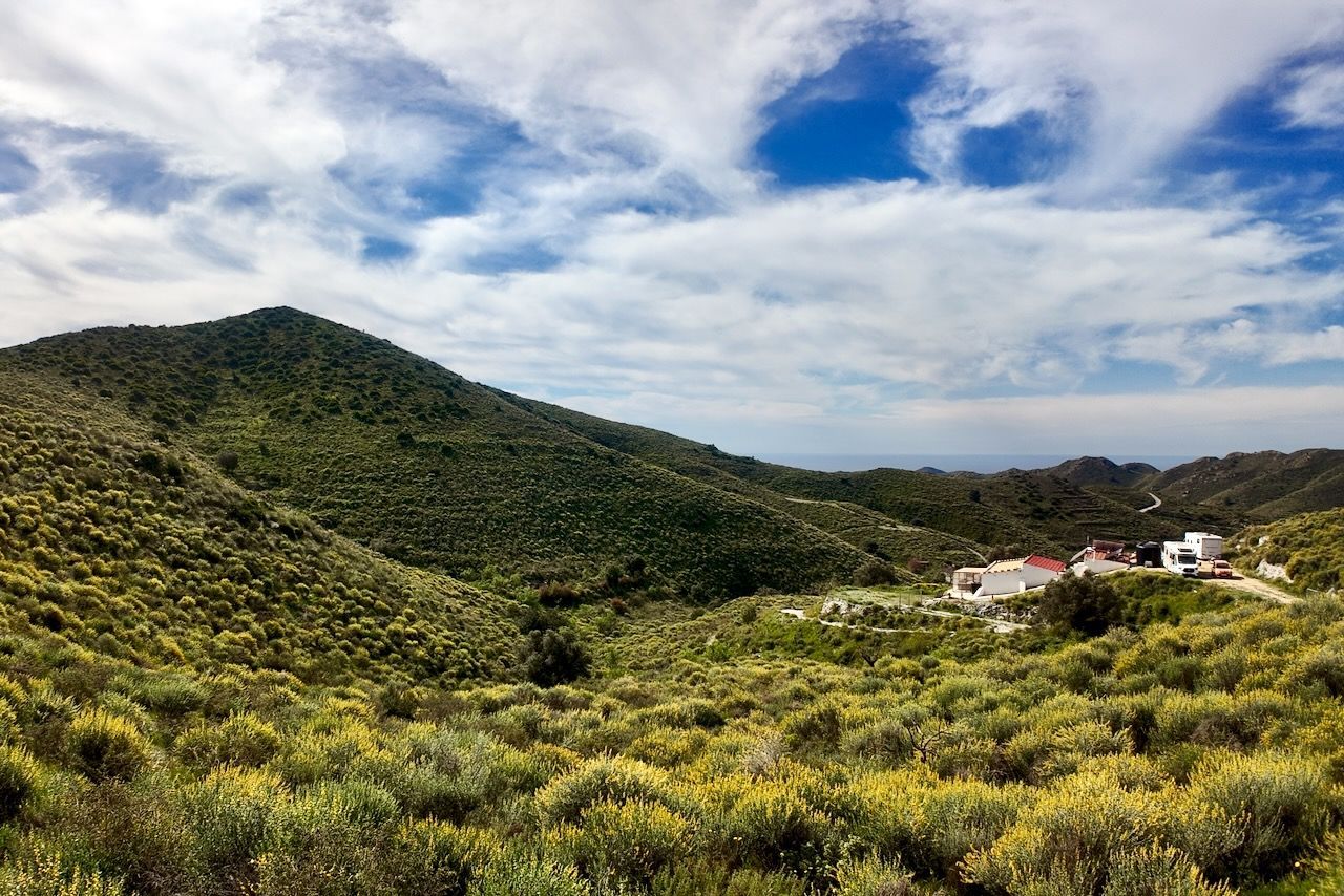 Glooiende heuvels bedekt met groene struiken onder een helderblauwe hemel, met een klein groepje witte huizen verscholen in het dal.