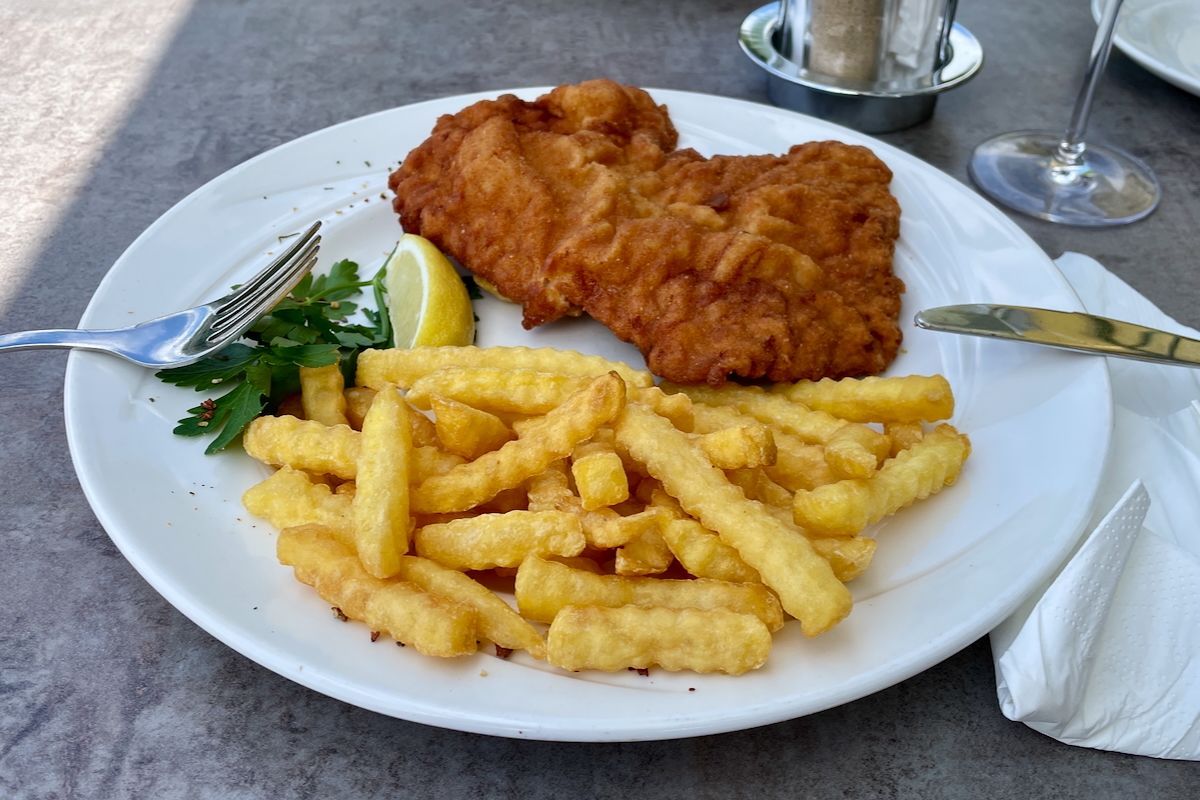 Wiener snitzel Een bord met eten met frietjes en schnitzel op een tafel.
