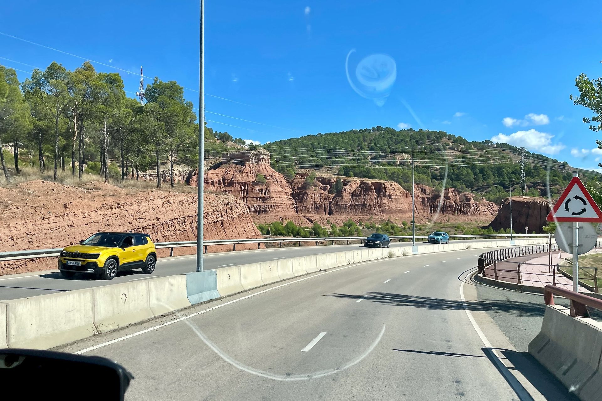 Gele Jeep op een weg met rode rotsformaties op de achtergrond, zonnige dag.