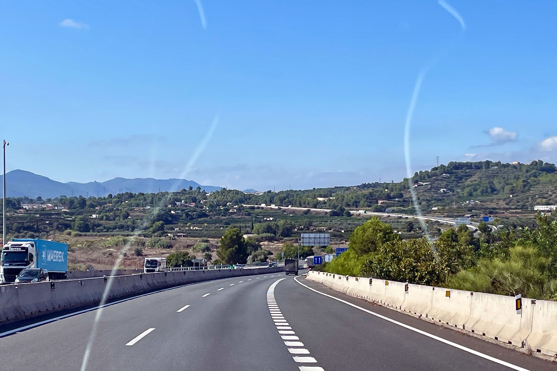 Snelweg met uitzicht op de bergen, blauwe lucht, vrachtwagens en betonnen obstakels.