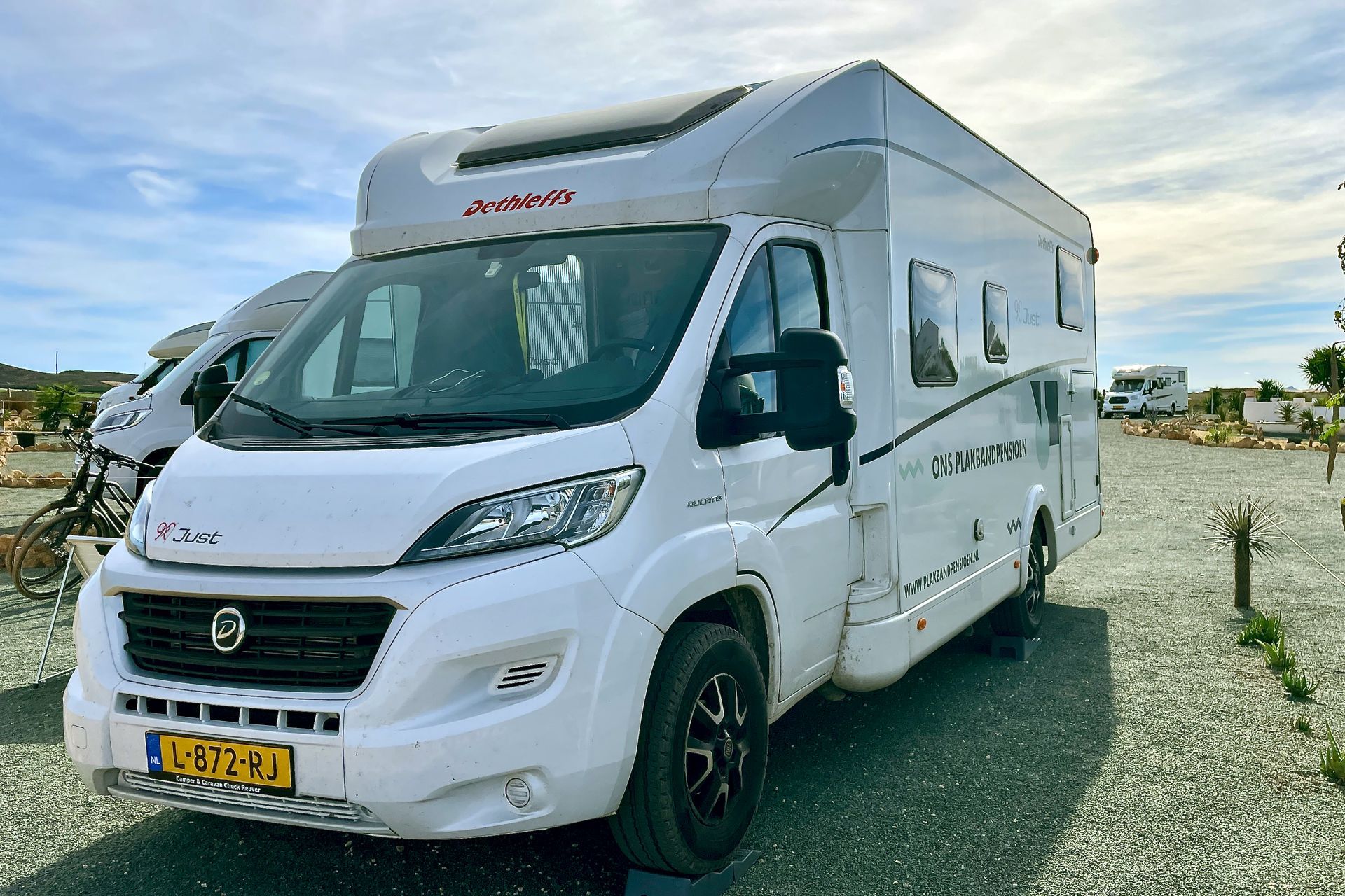 Witte camper geparkeerd op een grindterrein onder een blauwe lucht, kenteken LB-72-HJ.