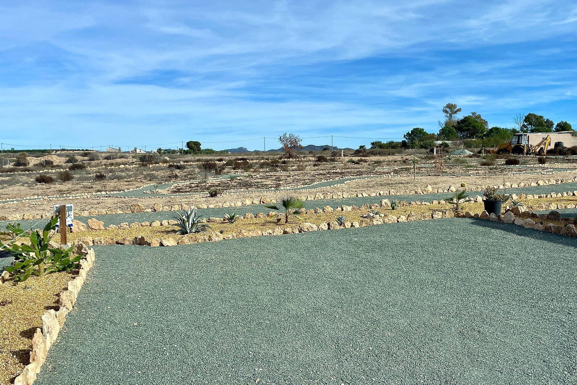 Uitzicht op een terrasvormig perceel met groene grind- en stenen randen onder een blauwe lucht.