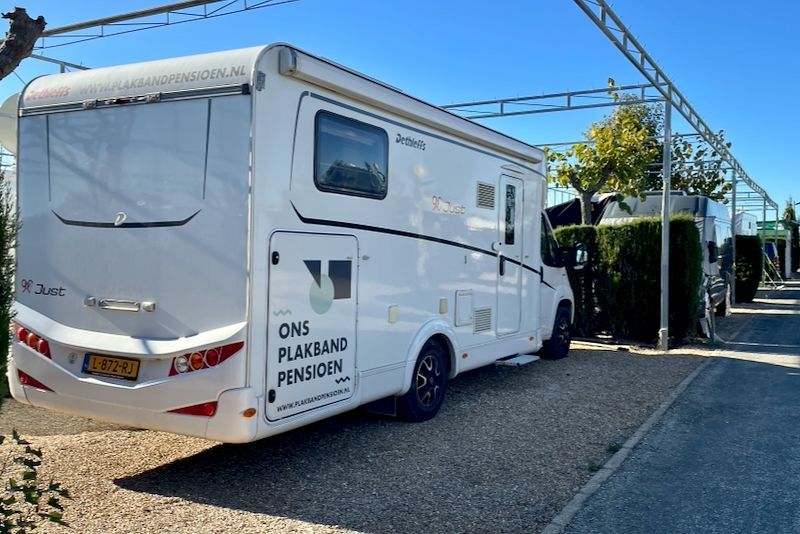 Witte camper geparkeerd onder een metalen luifel. Tekst op de zijkant: 