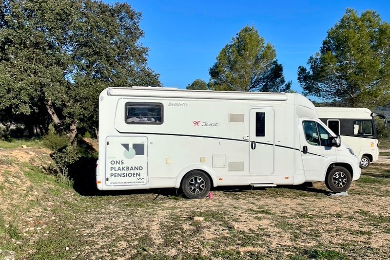 Witte camper geparkeerd op een grasveld, op een zonnige dag. Een andere camper is zichtbaar op de achtergrond.