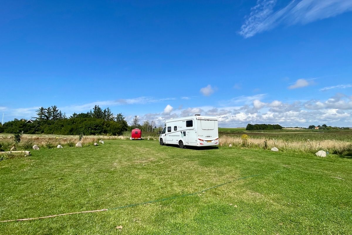 Vrijheid in Denemarken A white rv is parked in a grassy field on a sunny day.