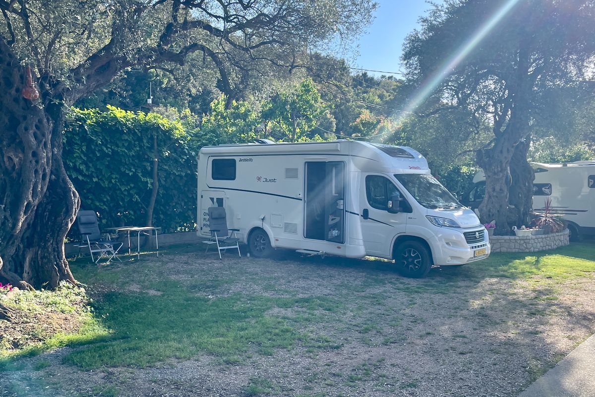 Onze overnachtingsplek Een witte camper staat geparkeerd in een grasveld naast een boom.