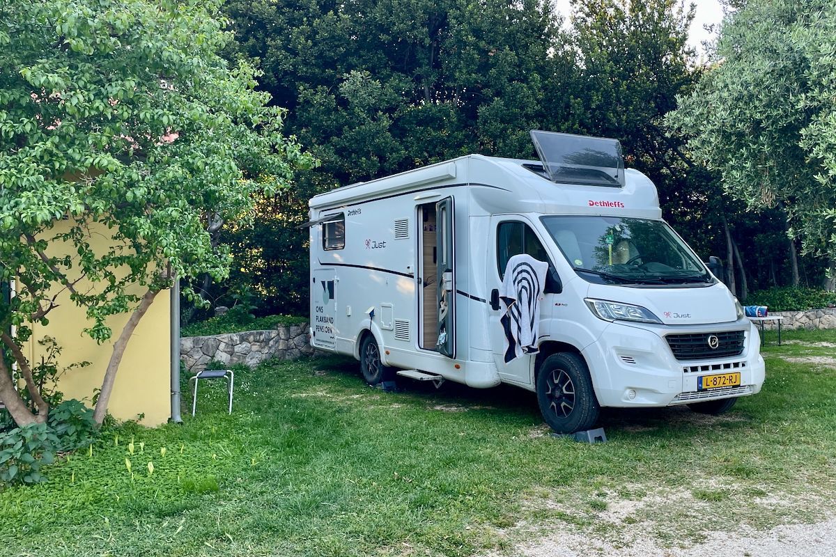 Overnachting op Camping Kate Een witte camper staat geparkeerd in een grasveld.