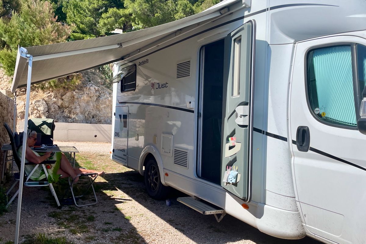 Ons plekje voor een nacht Een vrouw zit onder een luifel naast een camper.