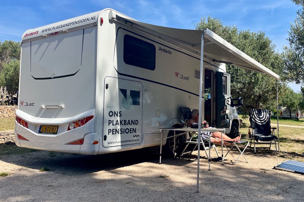 De luifel kan uit Een witte camper met luifel staat geparkeerd in een veld.